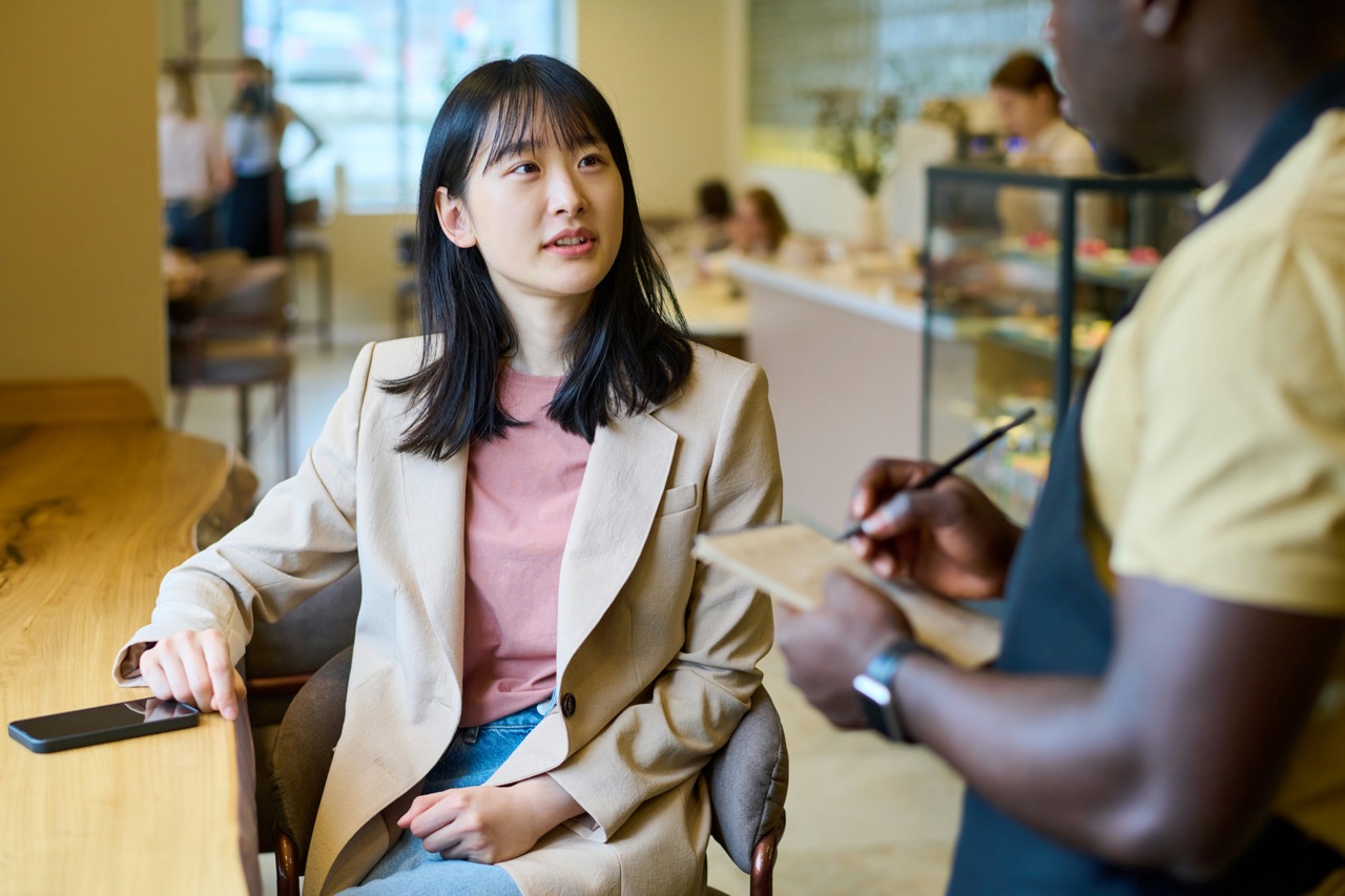 A woman sitting at a cafe table, speaking with a waiter who is taking her order