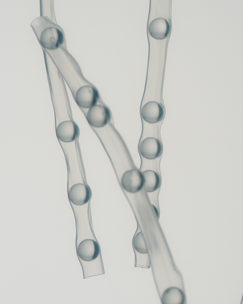 Close-up of thin, transparent tubes filled with round beads, floating against a plain background, giving a minimalistic, scientific or laboratory vibe