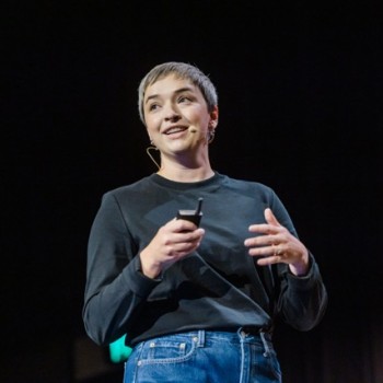 Georgia Rust speaks with confidence at Product Outlook, holding a clicker and engaging the audience with a thoughtful expression.