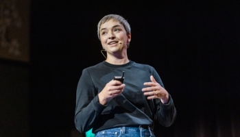 Georgia Rust speaks with confidence at Product Outlook, holding a clicker and engaging the audience with a thoughtful expression.