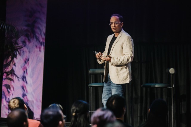 Vivek on stage at DO24, wearing a beige blazer and jeans, engaging the audience with a confident stance and expressive gestures during his talk.