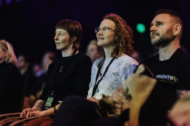 DO24 attendees immersed in a session, their expressions reflecting curiosity and engagement as they listen intently in the dimly lit event space.