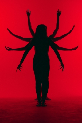 A silhouette of a person standing against a bright red background, with multiple arms extended in different positions behind them, creating a dramatic, surreal effect.