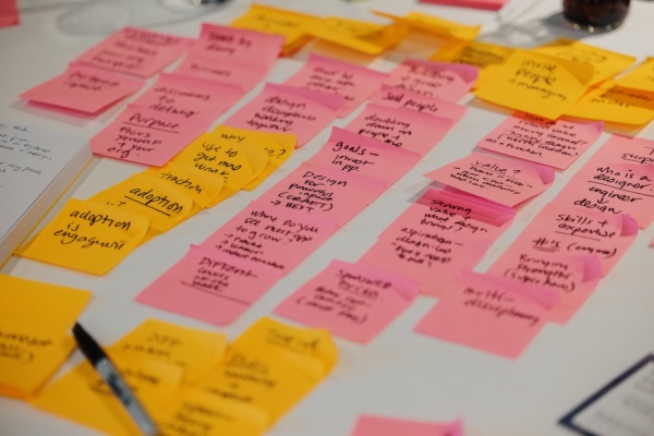 A close-up of a table covered with brightly colored sticky notes in pink and yellow, each containing handwritten brainstorming ideas. The notes are arranged in clusters, showcasing a collaborative and creative session. A pen and other materials are visible, adding to the dynamic and productive atmosphere.