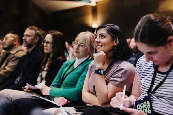 DO24 attendees engaged in a session, with some taking notes while others listen attentively, capturing a moment of curiosity and focus in the audience.