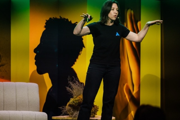 Tarra van Amerongen presents at Product Outlook 2025, gesturing expressively on stage against a vibrant, silhouetted backdrop.