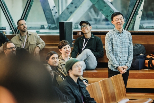 Audience members at Design Outlook 2023 seated in wooden-tiered seating, smiling and reacting during a session.