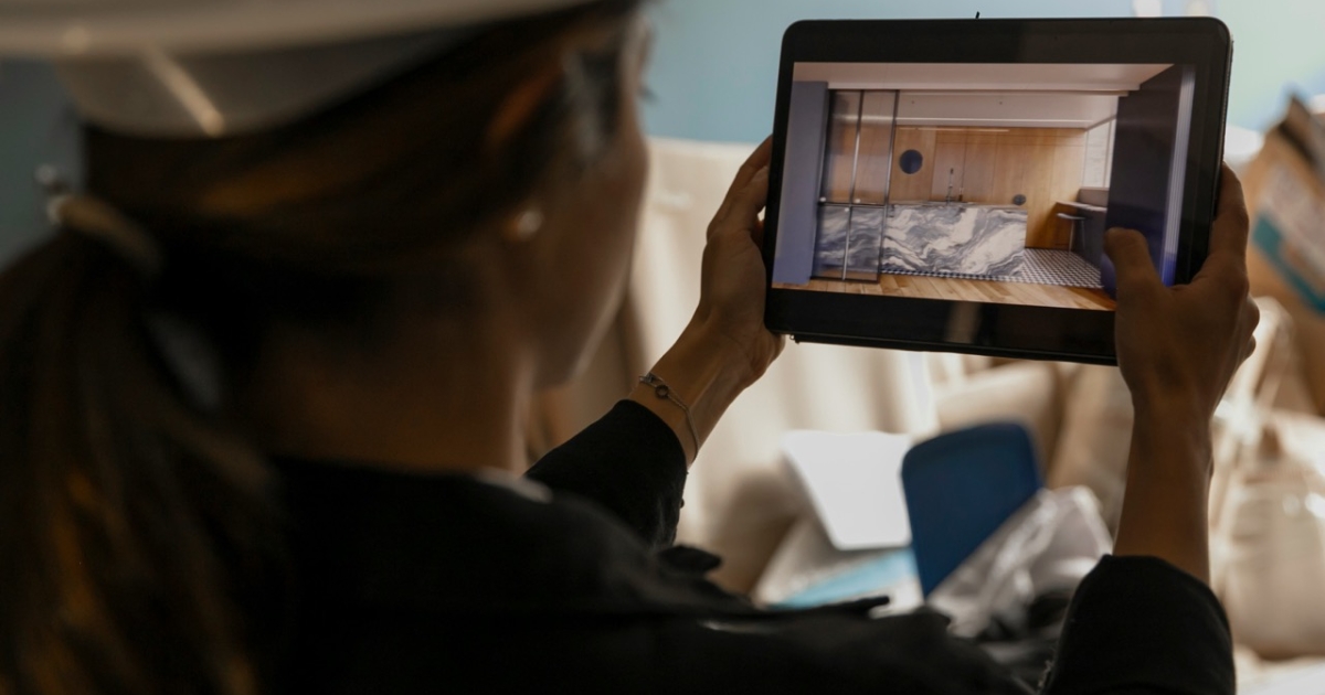 A person wearing a hard hat using a tablet to view a digital image of a room interior with a marble design