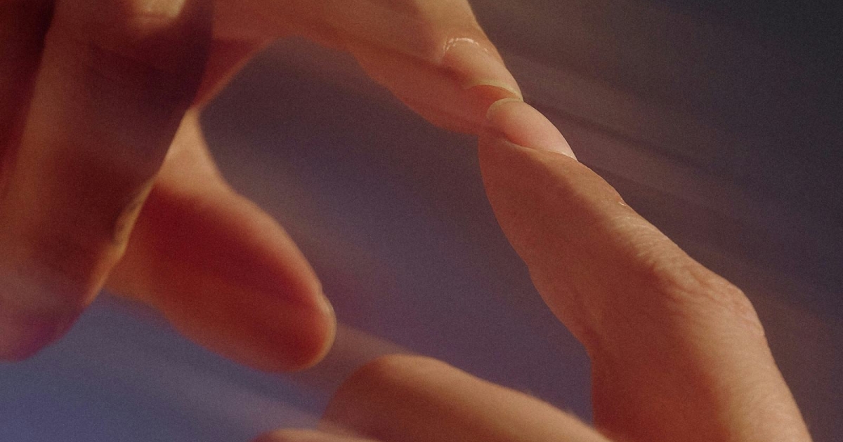  Two hands reaching toward each other with fingers almost touching, creating a gentle and soft image. The light creates a blurred effect on the hands, enhancing a feeling of motion