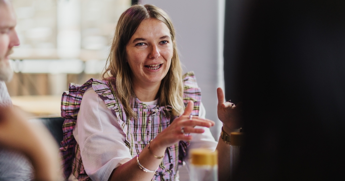 A design leader speaking and gesturing during a roundtable discussion at the DO Design Leadership event in Melbourne, 2024. She appears engaged and expressive, contributing to the collaborative atmosphere of the gathering.