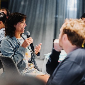 Bronwen van den Merwe speaks with a smile during a roundtable session at Design Leadership 2023, microphone in hand and warmly engaging with the group.