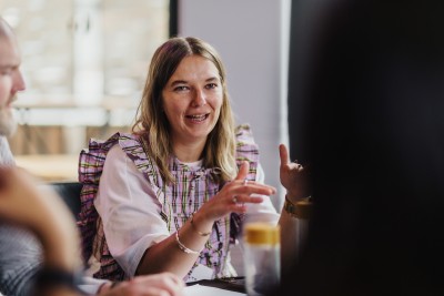 A design leader speaking and gesturing during a roundtable discussion at the DO Design Leadership event in Melbourne, 2024. She appears engaged and expressive, contributing to the collaborative atmosphere of the gathering.